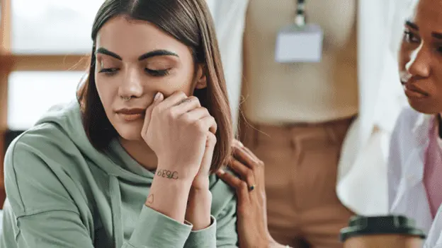 Two women talking, one showing signs of emotional exhaustion, symbolizing recovery burnout.